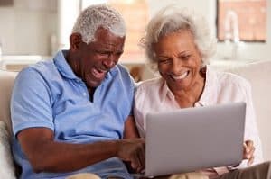 Senior,Couple,Sitting,On,Sofa,At,Home,Together,Using,Laptop